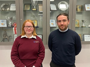 Grianghraf de scoláire agus múinteoir os comhair cófra trófaithe